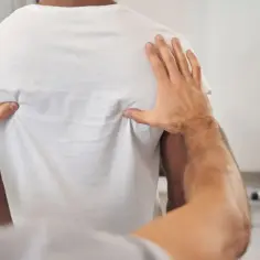 Fizjoterapeuta bada górną część pleców pacjenta, szukając przyczyny bólu pleców u góry.