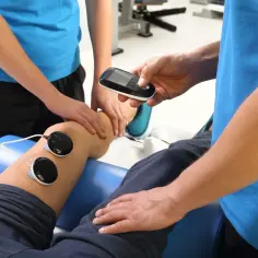 Fizjoterapeuta z urządzeniem do fonowania przygotowuje pacjenta do zabiegu na kolano.