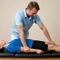 Fizjoterapeuta wykonuje masaż izometryczny na nogach pacjentki leżącej na kozetce.