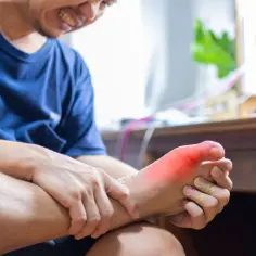 Mężczyzna trzyma stopę z zaczerwienionym palcem, cierpiąc z bólu.