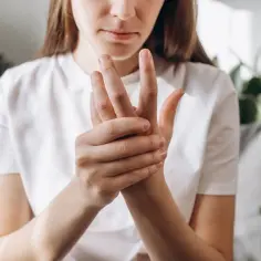 Kobieta masuje lewą dłoń, odczuwając ból lewej ręki.