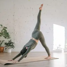 Kobieta w zielonym stroju wykonuje pozycję psa z jedną nogą w górze, pogłębiając stretching.