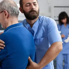 Fizjoterapeuta pomaga pacjentowi z bólem lędźwi. W tle widać szkielet i drugą pielęgniarkę.