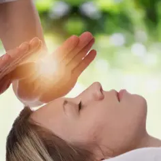 Dłonie terapeuty nad głową kobiety, emanujące jasnym światłem.