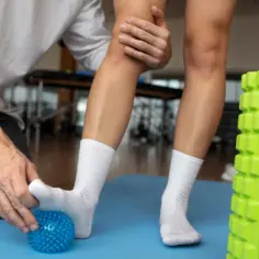 Fizjoterapeuta masuje stopę pacjenta niebieską piłeczką do masażu.