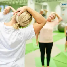 Grupa osób wykonuje ćwiczenia rozciągające szyję w sali rehabilitacyjnej.