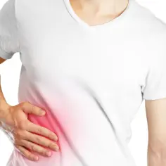 Osoba w białej koszulce odczuwa tępy ból w prawym boku nad biodrem, co sugeruje problem zdrowotny.