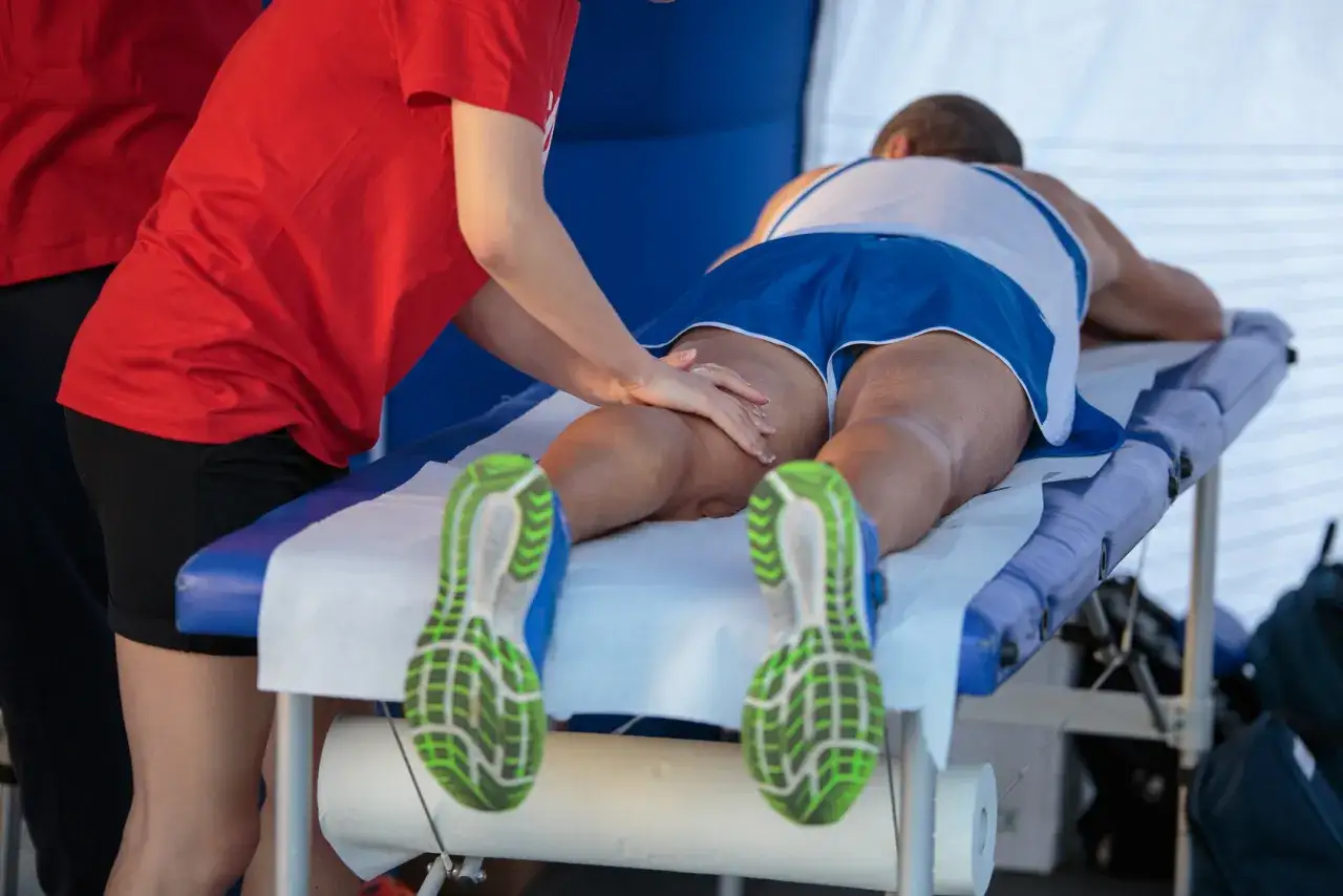 Masaż sportowy ud biegacza po zawodach. Fizjoterapeuta pracuje nad mięśniami.