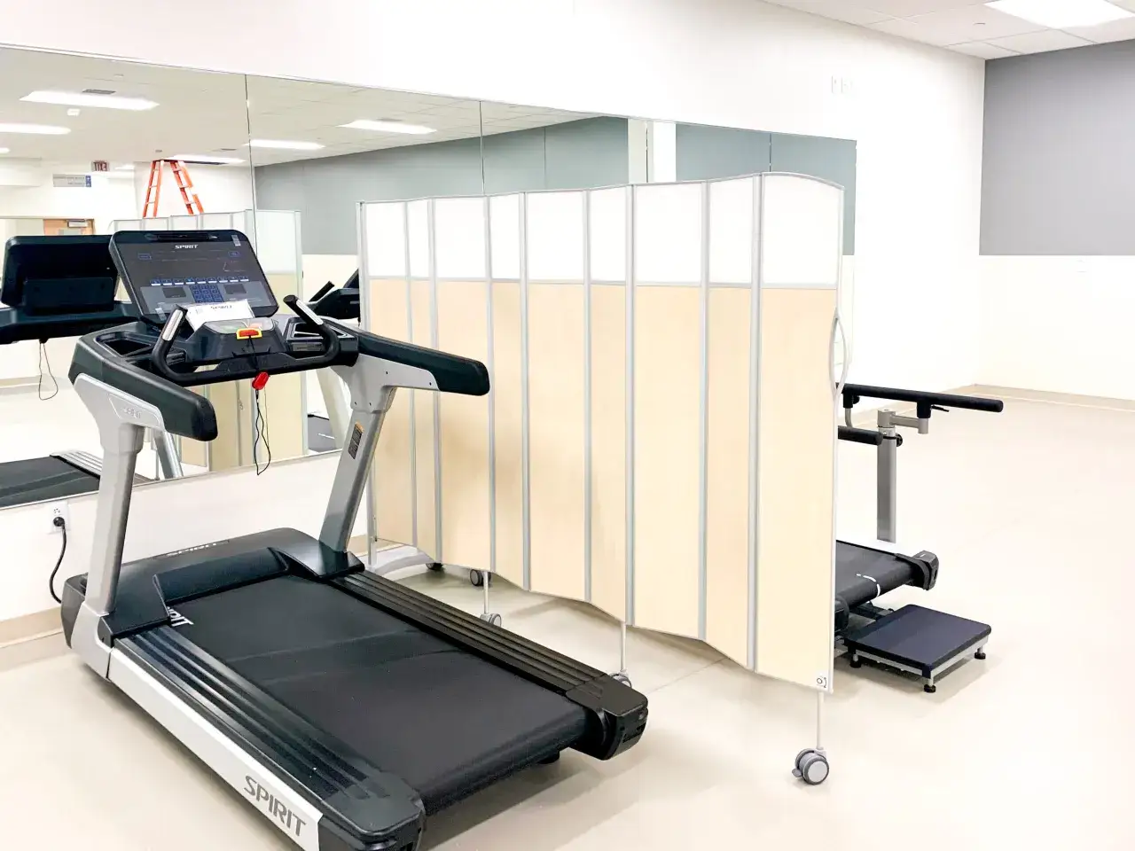 Sala do rehabilitacji z bieżnią i parawanem. Fizjoterapia co to? To powrót do sprawności.