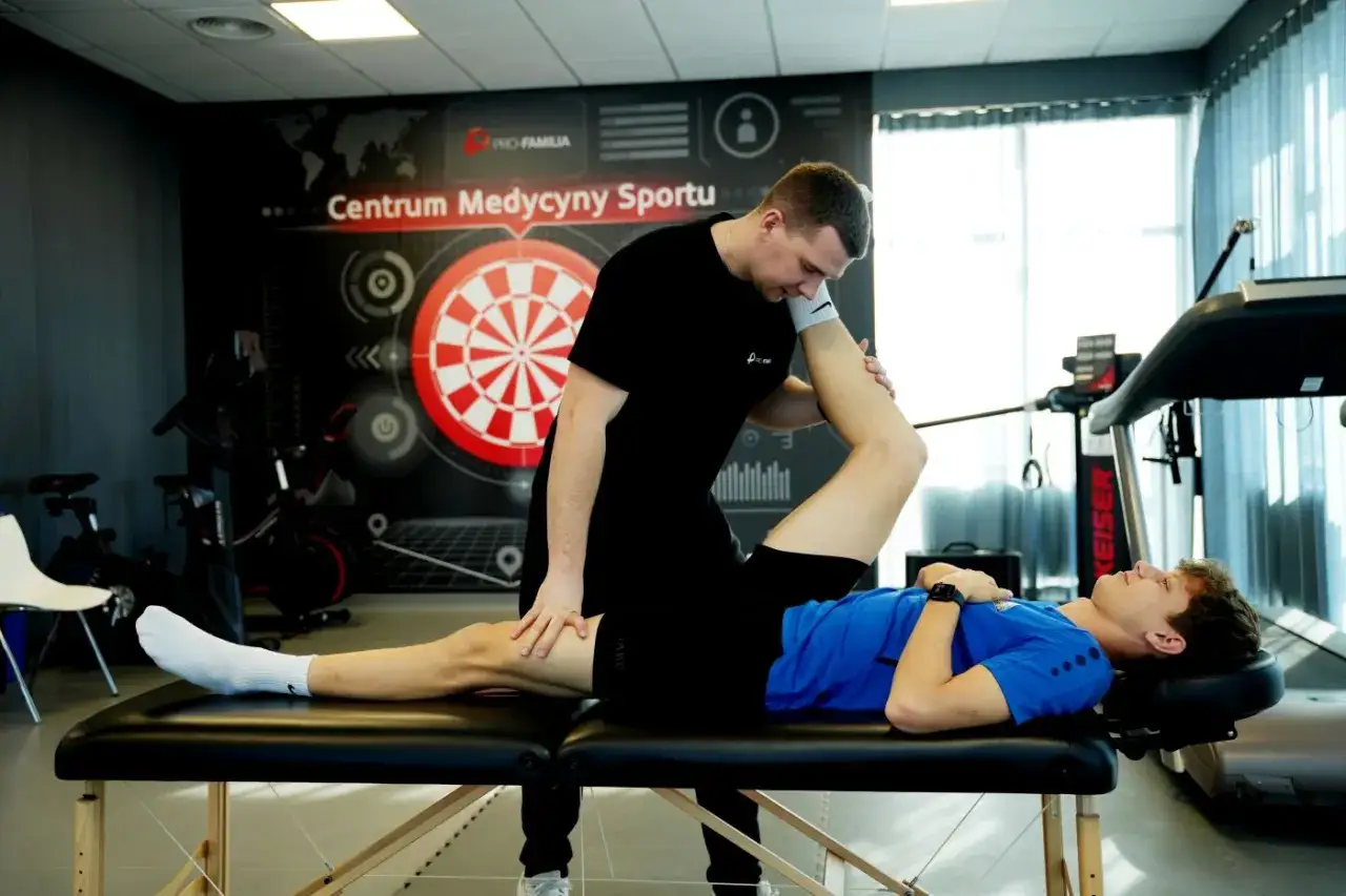 Lekarz sportowy wykonuje badanie fizjoterapeutyczne młodego sportowca na kozetce w centrum medycyny sportowej.